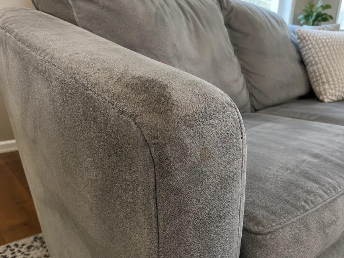 Body-oil stain on the armrest of a gray microfiber couch before cleaning